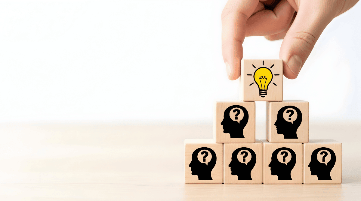 A hand places a wooden block with a lightbulb icon atop a pyramid of blocks, illustrating the path to Strategic Intelligence & Enablement through clarity.